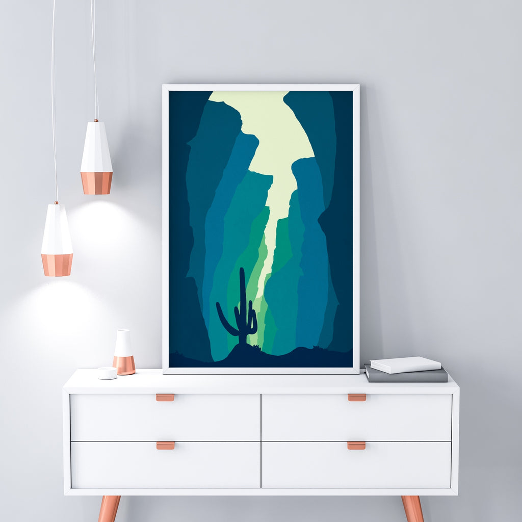 A saguaro cactus rises to the light above a canyon painted in blues and greens and a cream desert sky.